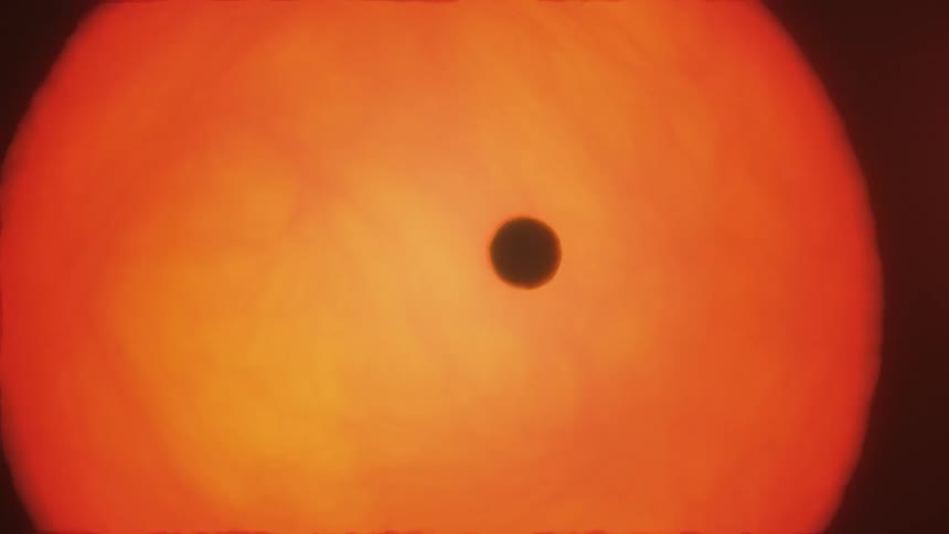 A small dark astronomical object moves in front of a large sun in outer space