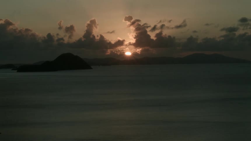 Sun setting over water with dark clouds moving across the sky