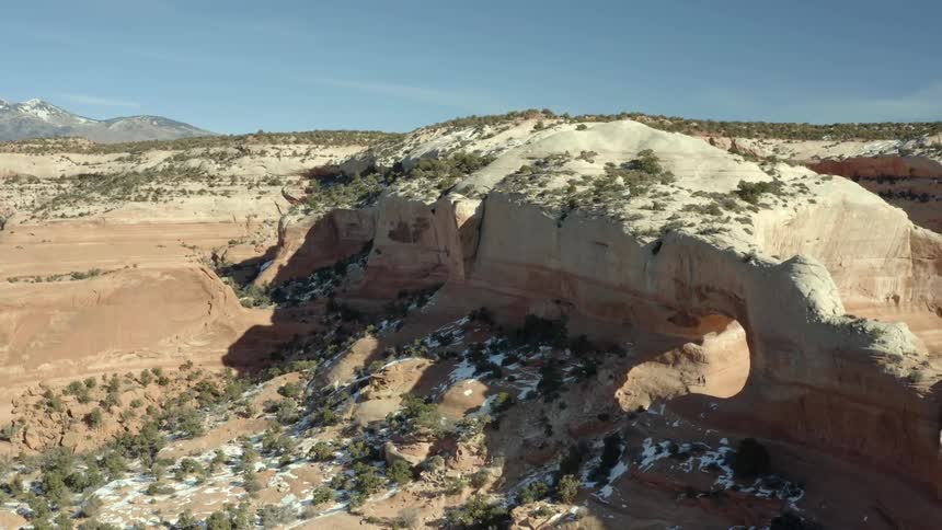 Aerial view of people standing under a natural rock arch in the desert