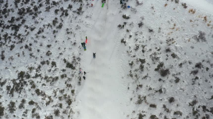 A group of people having fun riding ice slides on the side of a snow covered hill at winter