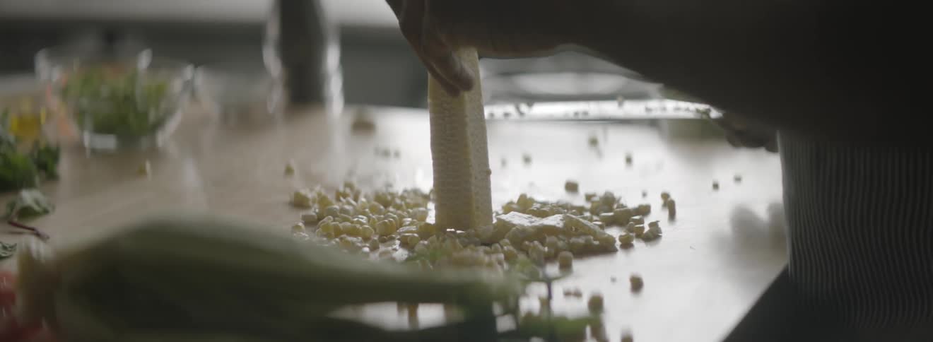 A man cuts corn off the cob in a kitchen