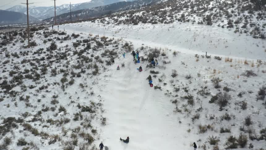 A group of people having fun riding ice slides on the side of a snow covered hill at winter