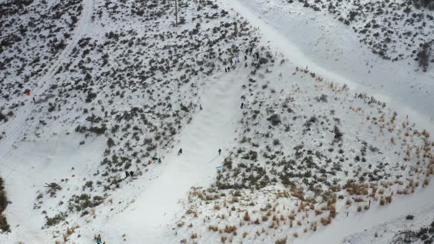 A person slides down a snow covered slope as others watch and wait their turn
