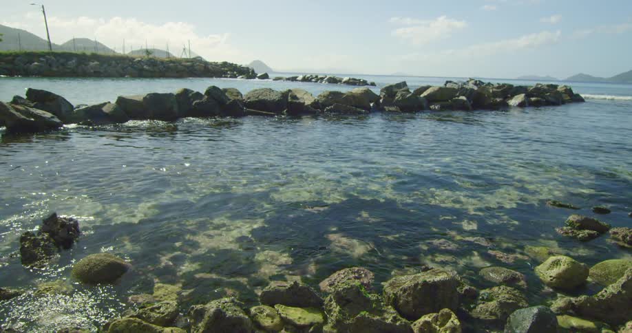 A rocky shore with water rippling with the sky and clouds in the background