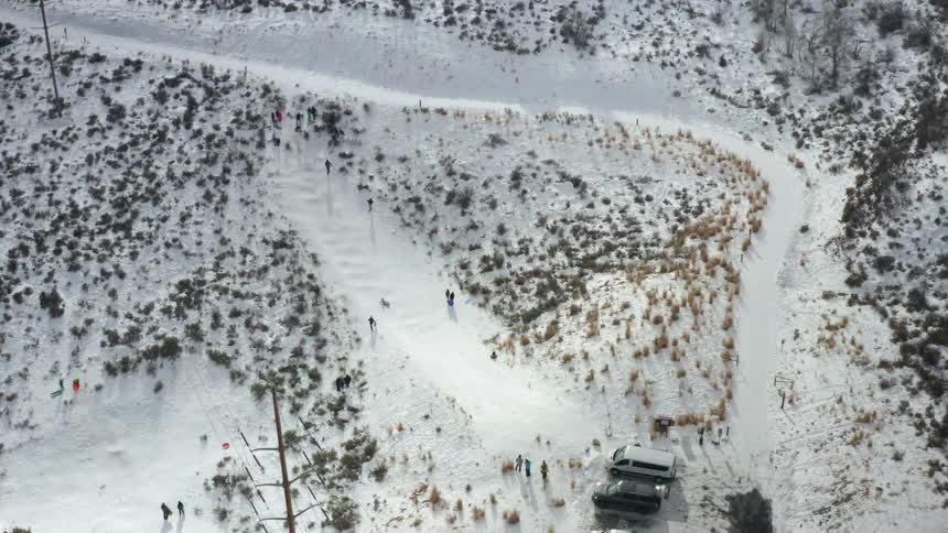 A person sliding down a snowy slope on a sled with other people standing and walking