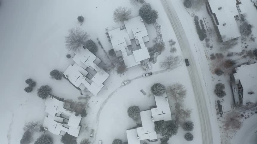 Aerial view of cars driving down a snow covered street in a neighborhood