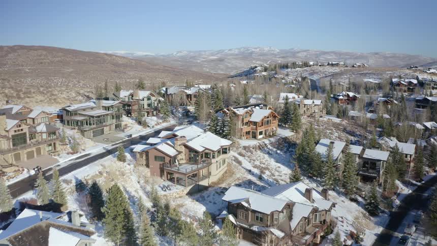 A town with snow covered houses trees and roads with a mountain range sky and clouds in the background