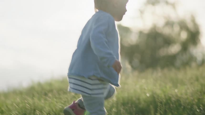 A child walking on a grassy field with trees the sky and clouds in the background