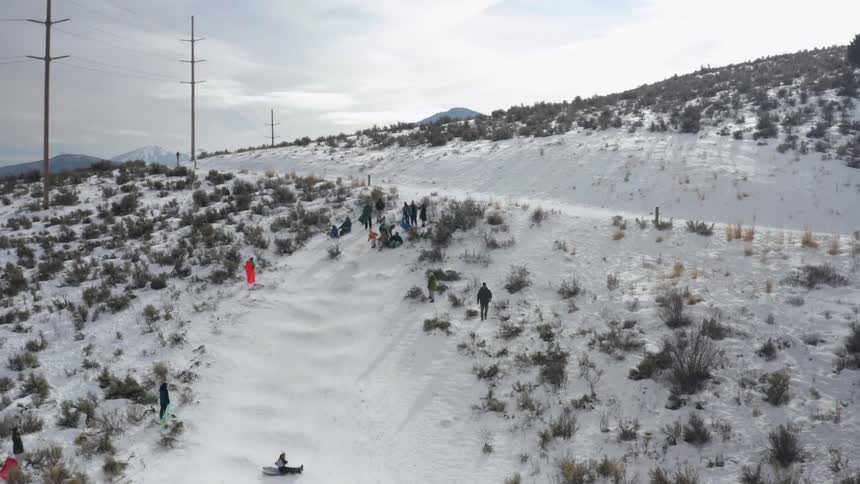People sled and slide down a snow covered slope while others watch and wait their turn