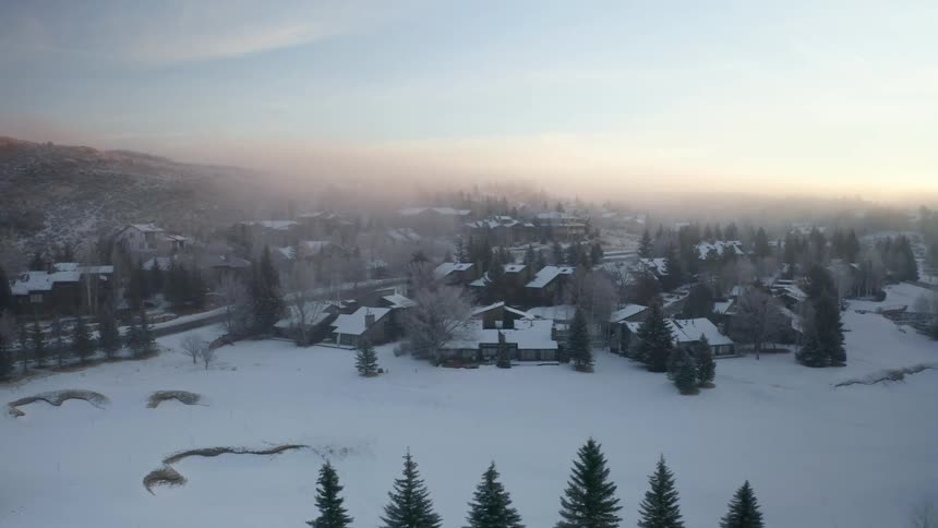 A town with houses roads with vehicles and trees covered in snow