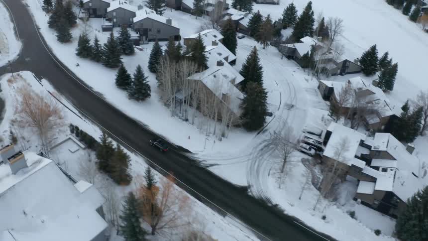 A vehicle driving on a road surrounded by trees snow and houses