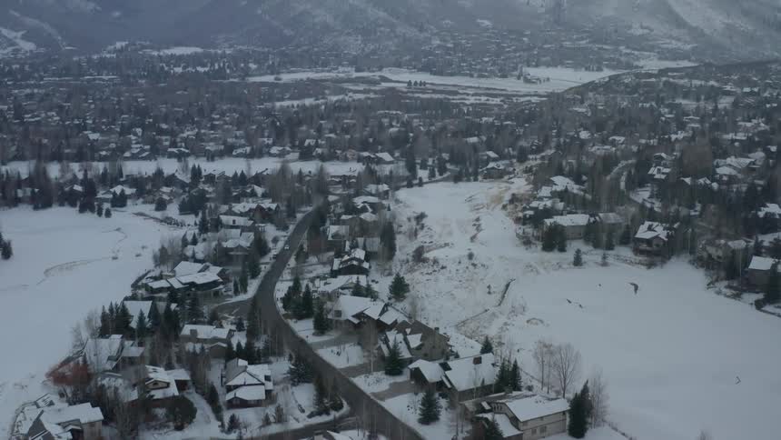 An aerial view of a neighborhood covered in snow pans up to a mountain range at daytime
