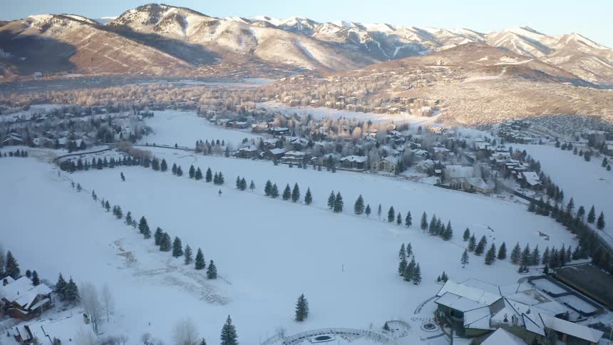 A town with snow covered houses trees and roads with a mountain range sky and clouds in the background
