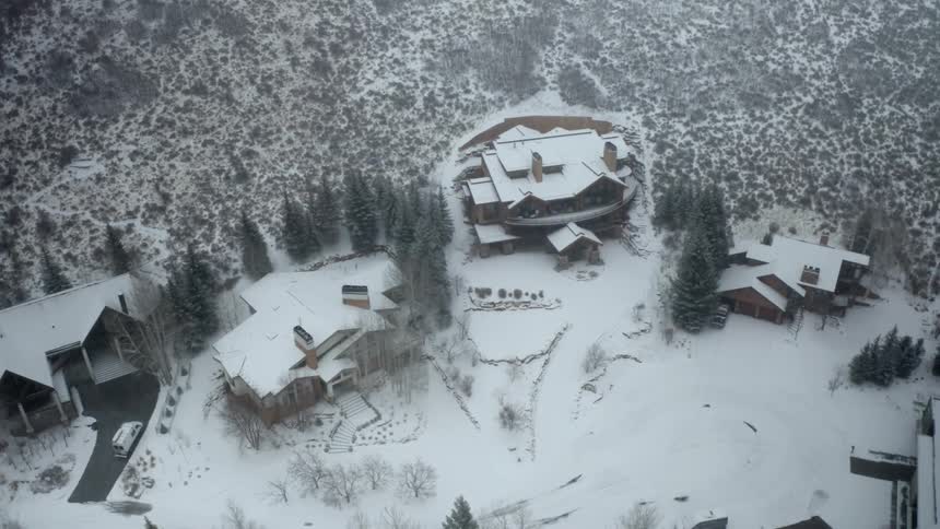 A truck pulls up to and enters the garage of a house at the base of a large hill on a snowy winter day