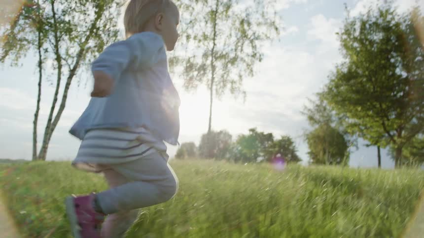 A toddler girl running through grass outside on a sunny summer day