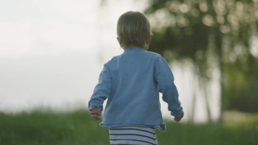 A child walking and running on a grassy field with the sky and clouds in the background