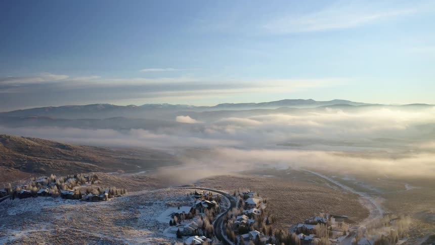 A road lined with small buildings winds through a foggy field covered in light snow on a winter day