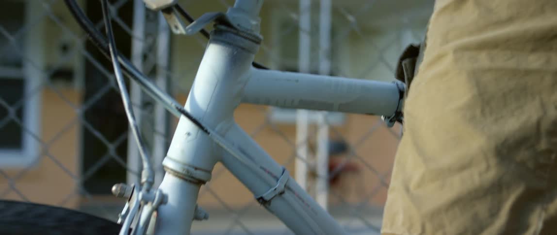 Man pushing a bicycle near a wire fence with a beware dog sign on it
