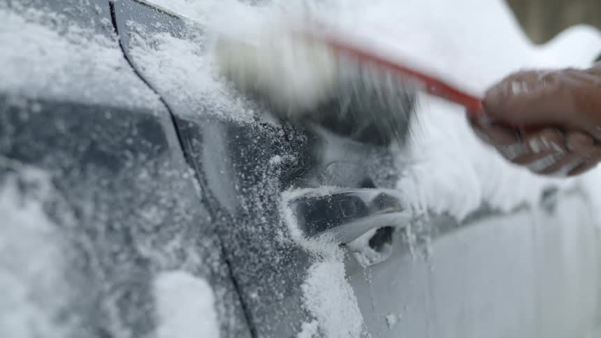 A person with gloves removing snow with a brush from a vehicles doorknob