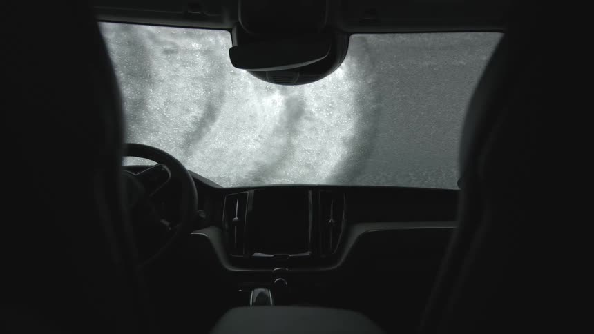 A person sweeps snow off a car windshield