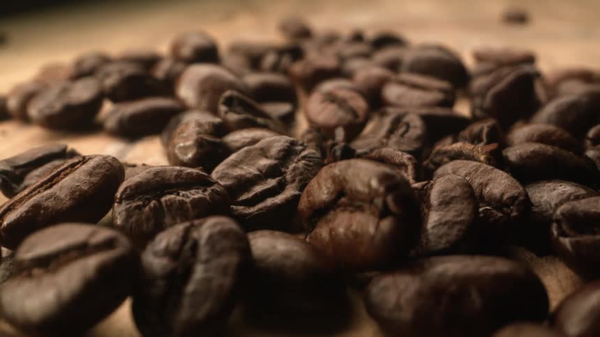 Brown roasted coffee beans falling and bouncing on wooden table