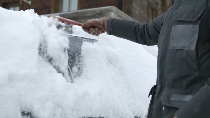 A person brushes snow off their vehicle outside their home