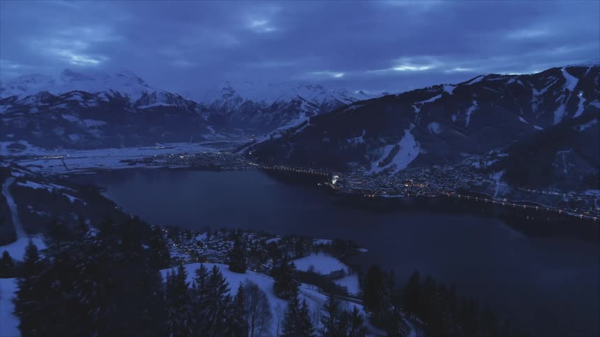 Aeral view of a small town on the banks of a lake in the snow covered mountains at evening
