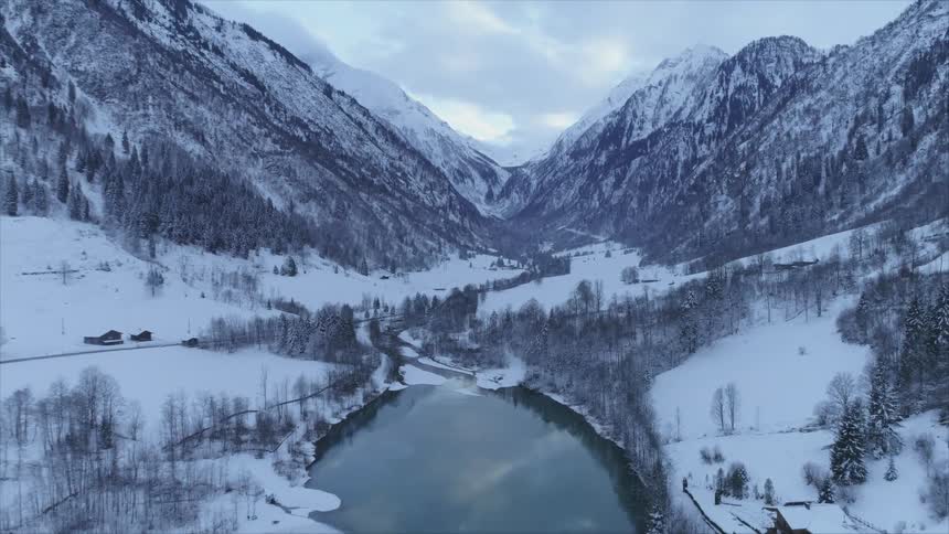 An aerial view of a lake surrounded by snowy mountains in nature on a winter day