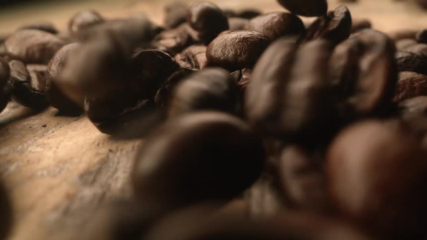 Brown roasted coffee beans bouncing on wooden table