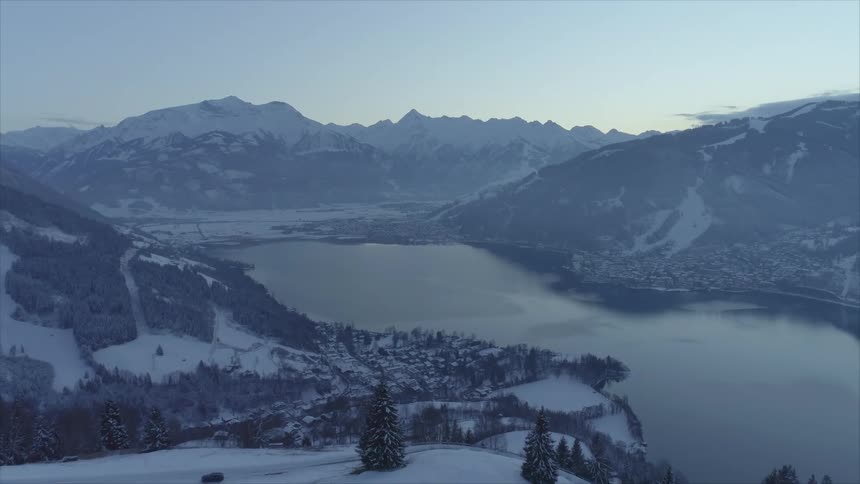 Snow covered mountain valley with a lake and many trees around