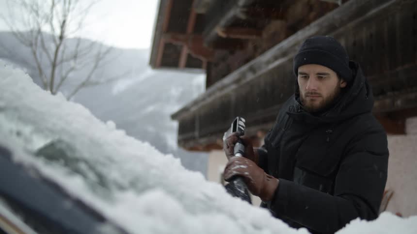 A man with a brush cleaning snow from a vehicle windshield