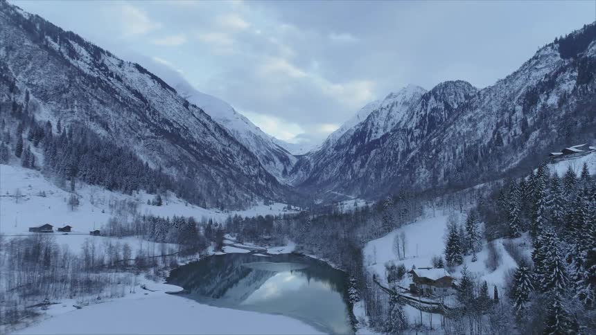 An aerial view of a lake surrounded by snowy mountains in the wilderness