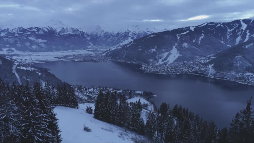 Snow covered mountain valley with a lake and many trees around