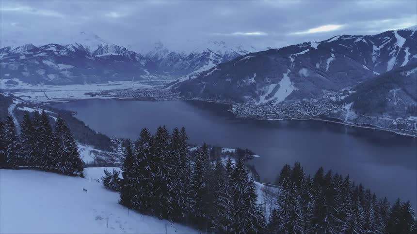 Snow covered mountain valley with a lake and many trees around under a cloudy sky