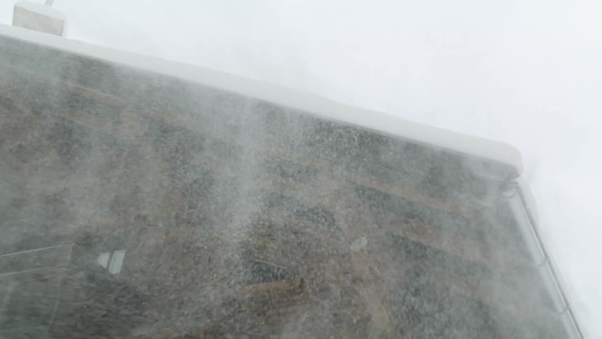 Snow swirling and blowing around a house