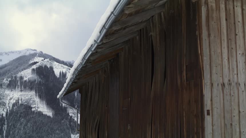 A small wood hut surrounded by snowy mountains on a cloudy winter day
