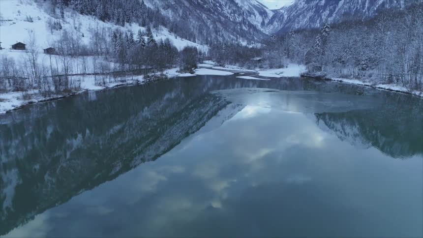A lake surrounded by trees with a snowcovered mountain range the sky and clouds in the background