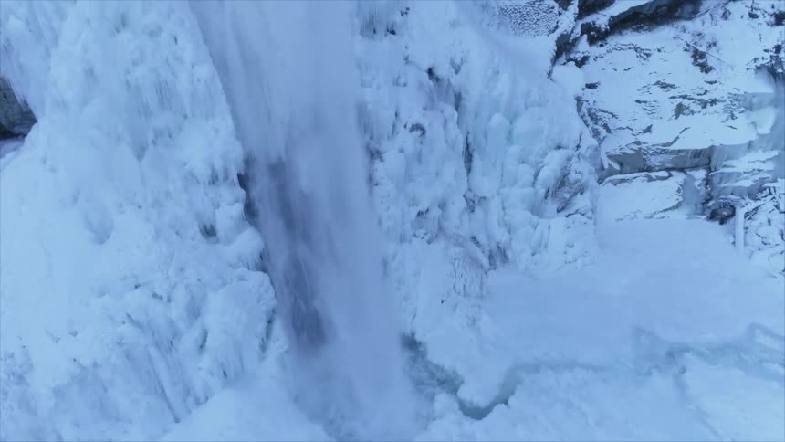 Water flows down an ice and snow covered rock face into a hole in the ice below