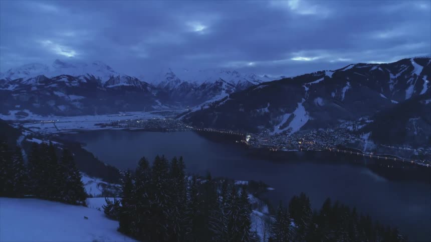 A small town around a lake in a snowy mountain valley on a cloudy evening