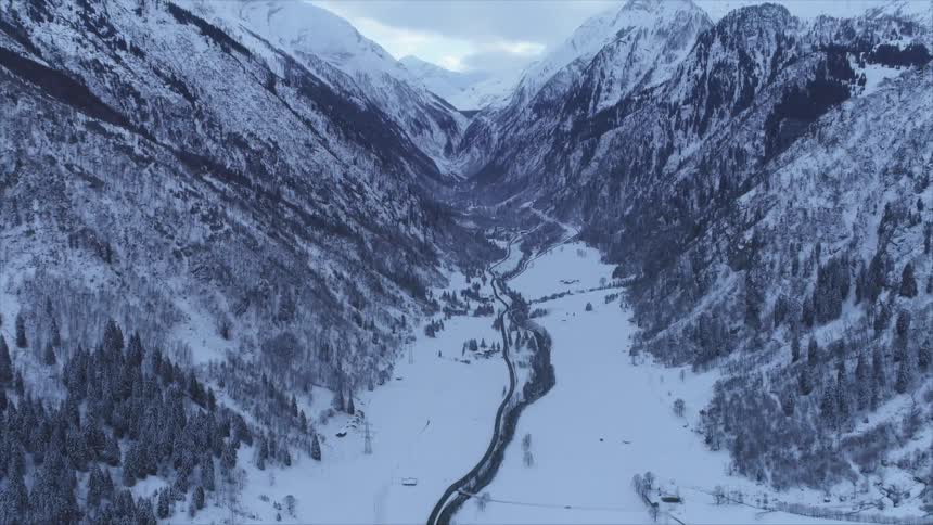 Roads surrounded by snow and trees in a valley between mountain ranges with the sky and clouds in the background