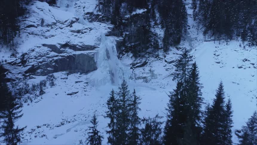 Water falls down a snow covered cliff in a woodland in the evening
