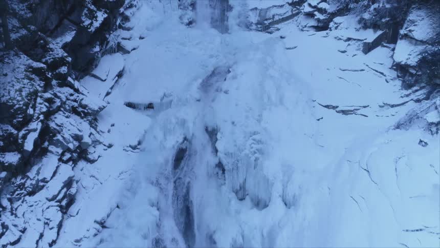 A waterfall flowing over a snowy cliff in the wilderness