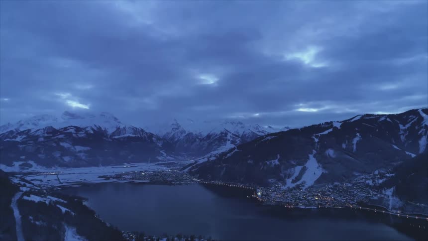 Lights from a town at the base of a mountain twinkle and reflect on the placid surface of the lake