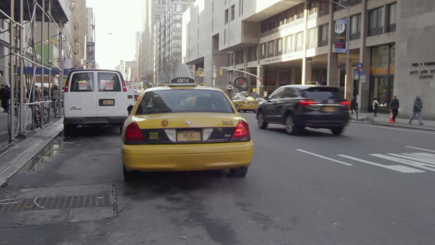 A taxi departs in a busy city street with pedestrians walking and bicyclist