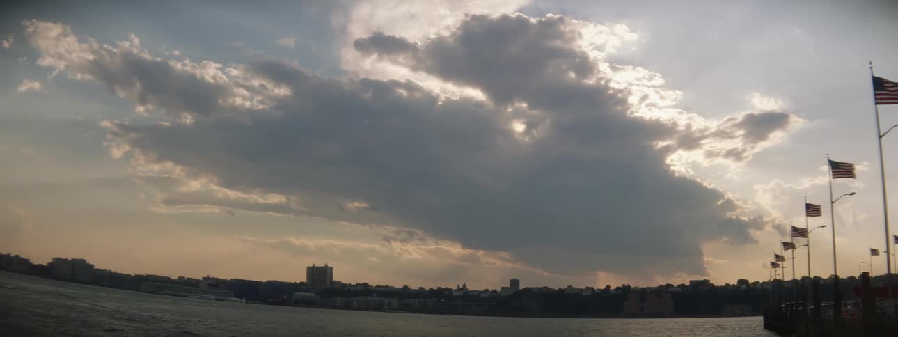 A pier with american flags next to a body of water with the sky and clouds in the background
