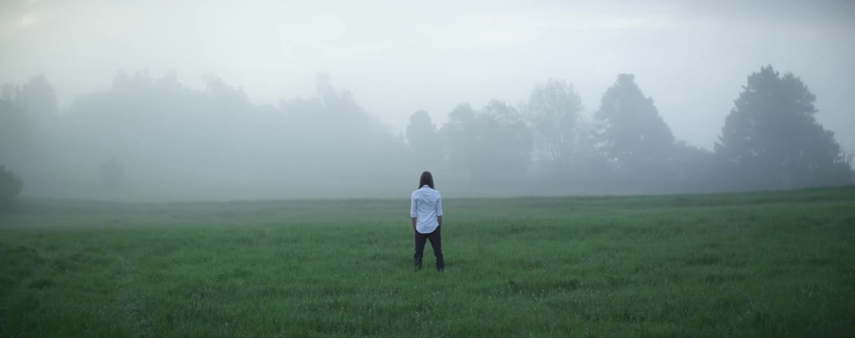 A person standing on a grassy field with trees the sky and clouds in the background