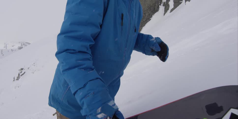 A man carrying a snowboard climbs a steep, snowy hill