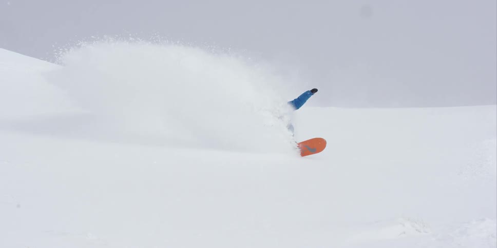 A snowboarder kicks up a large plume of snow as he goes downhill