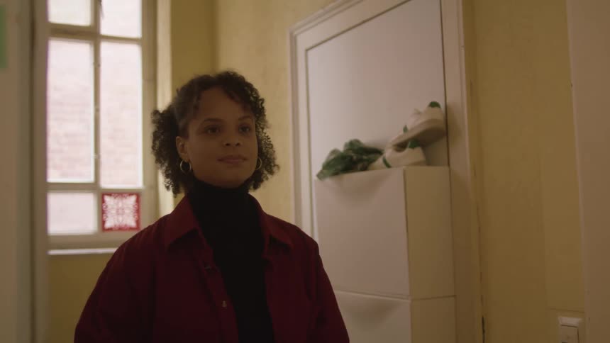 Young woman wearing a red jacket waiting to be invited into a house
