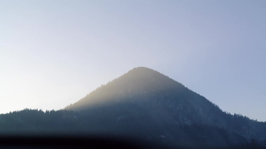 A vehicle driving with a windshield with a mountain range the sky and clouds in the background